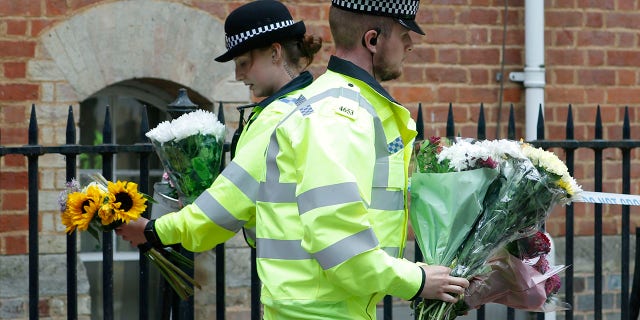 Police officers collecting flowers left at the Abbey gateway of Forbury Gardens on Sunday, one day after the stabbing attack. (AP Photo/Alastair Grant)