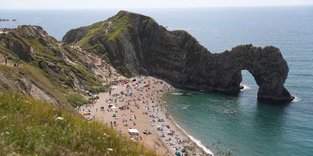 People relax on the beach of Durdle Door beach, as the public are being reminded to practice social distancing following the relaxation of coronavirus lockdown restrictions, near Lulworth in Dorset, England, Saturday May 30, 2020.