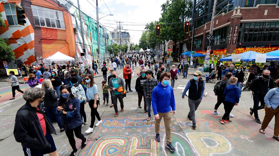 Visitors walk near a sign that reads "Welcome to CHOP," Sunday, June 14, 2020, inside what has been named the Capitol Hill Occupied Protest zone in Seattle.