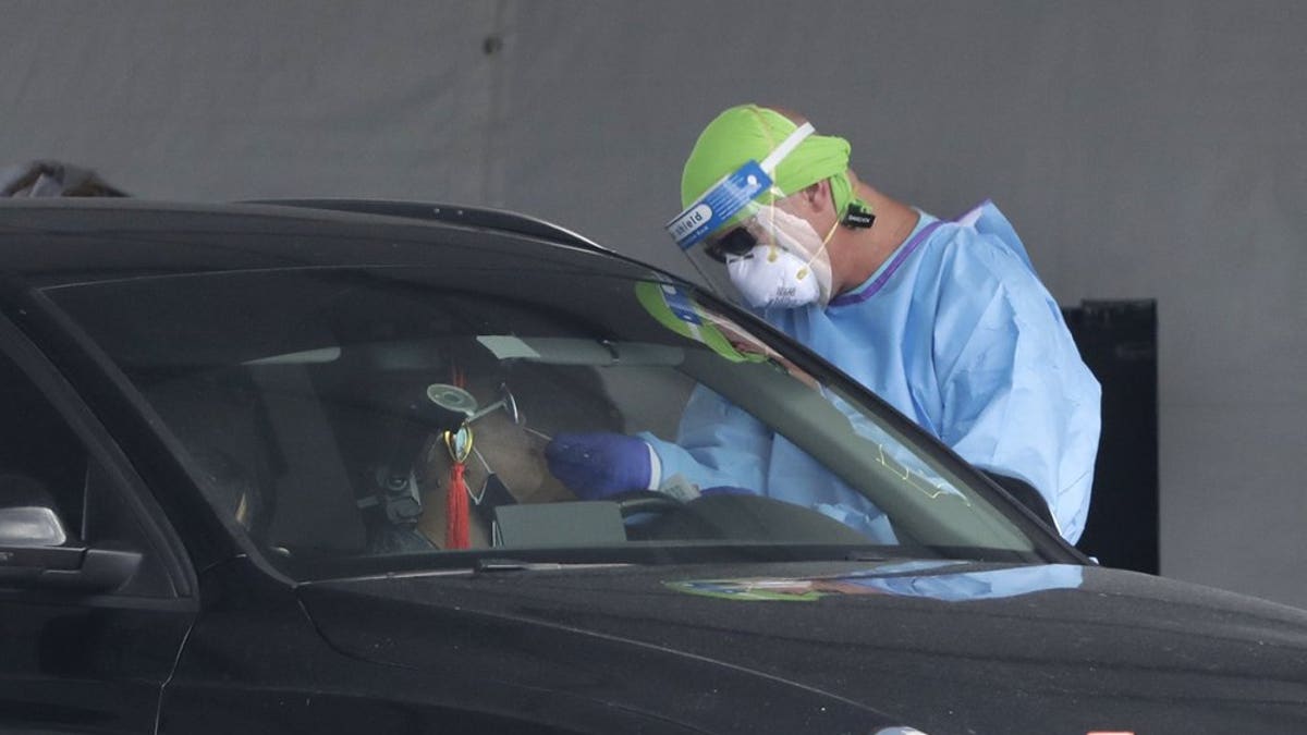 A healthcare worker takes a swab sample from a driver at a drive-through COVID-19 testing site outside Hard Rock Stadium, Wednesday, July 8, 2020, in Miami Gardens, Fla. Florida is one of the nation's hot spots for coronavirus.