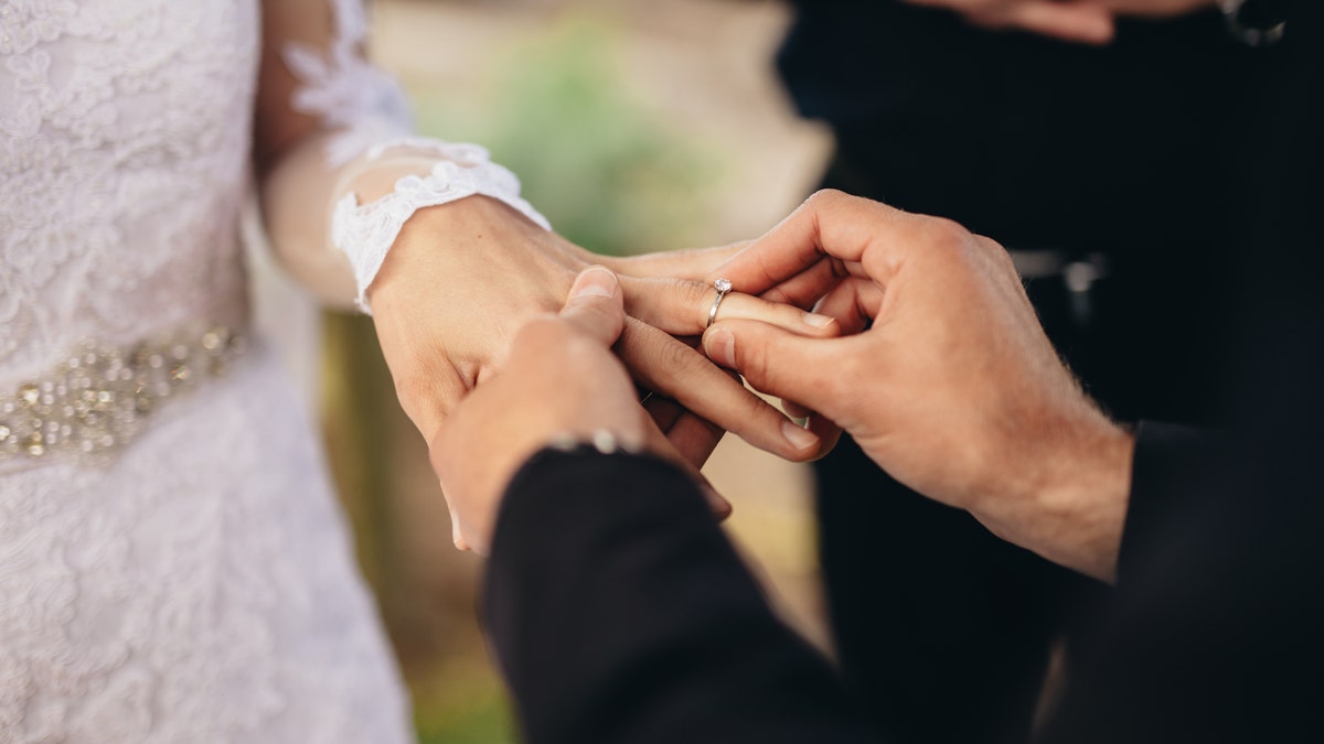 Closeup of groom placing a wedding ring on the brides hand. Couple exchanging wedding rings during a wedding ceremony outdoors.