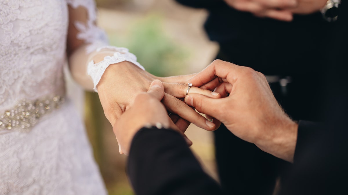 Closeup of groom placing a wedding ring on the brides hand. Couple exchanging wedding rings during a wedding ceremony outdoors.