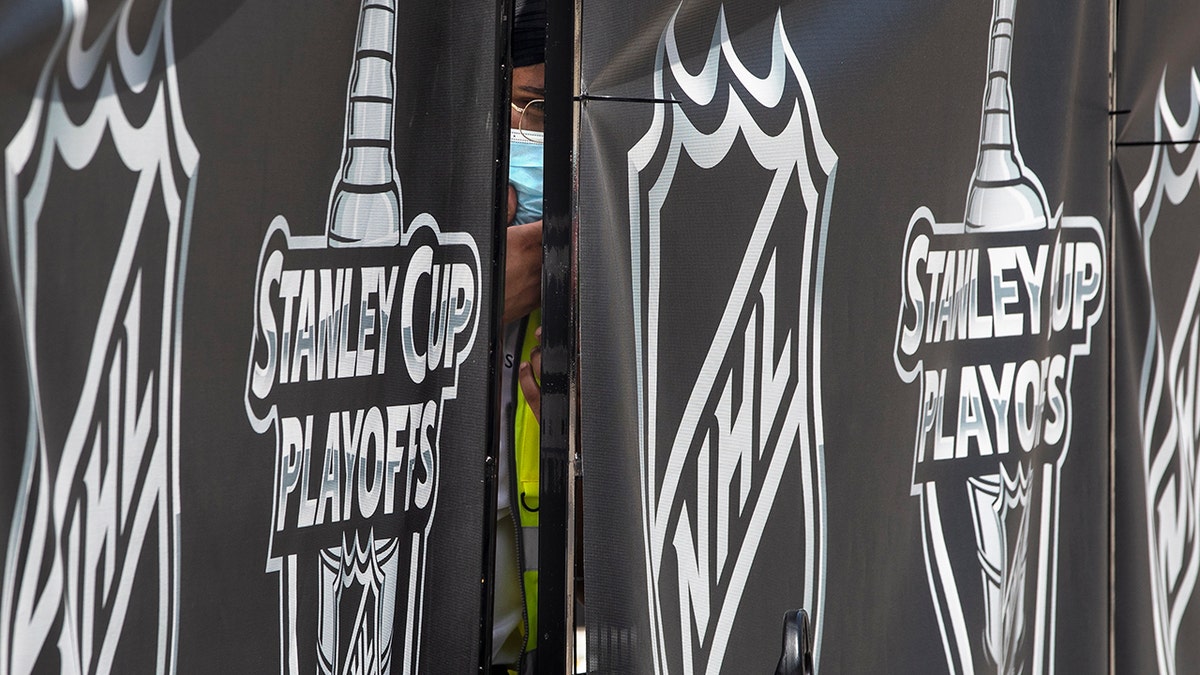 A security guard peers out from behind NHL-branded fencing at the entrance where players arrive at Toronto's Royal York hotel, which is acting as the "bubble" ahead of the return of the league's season following disruption due to the COVID-19 pandemic, Sunday, July 26, 2020. (Chris Young/The Canadian Press via AP)