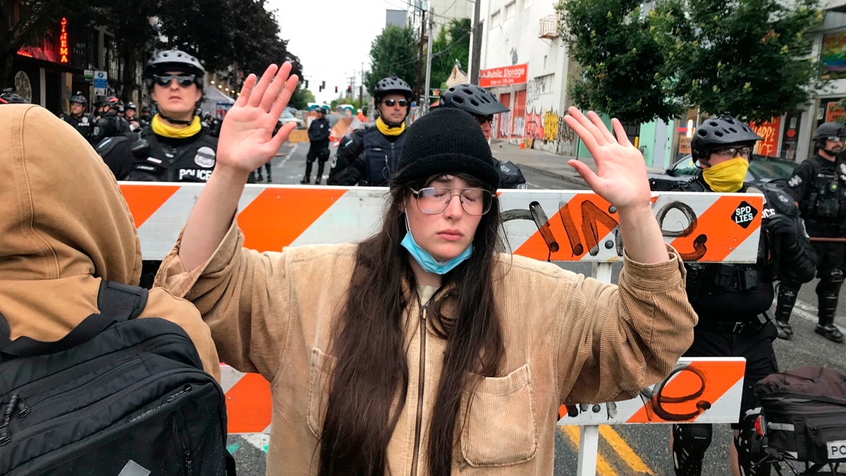 A protester stands with her hand up in front of a road blocked by Seattle police in the Capitol Hill Organized Protest zone early Wednesday. Police in Seattle have torn down demonstrators' tents in the city's so-called occupied protest zone after the mayor ordered it cleared. (AP Photo/Aron Ranen)