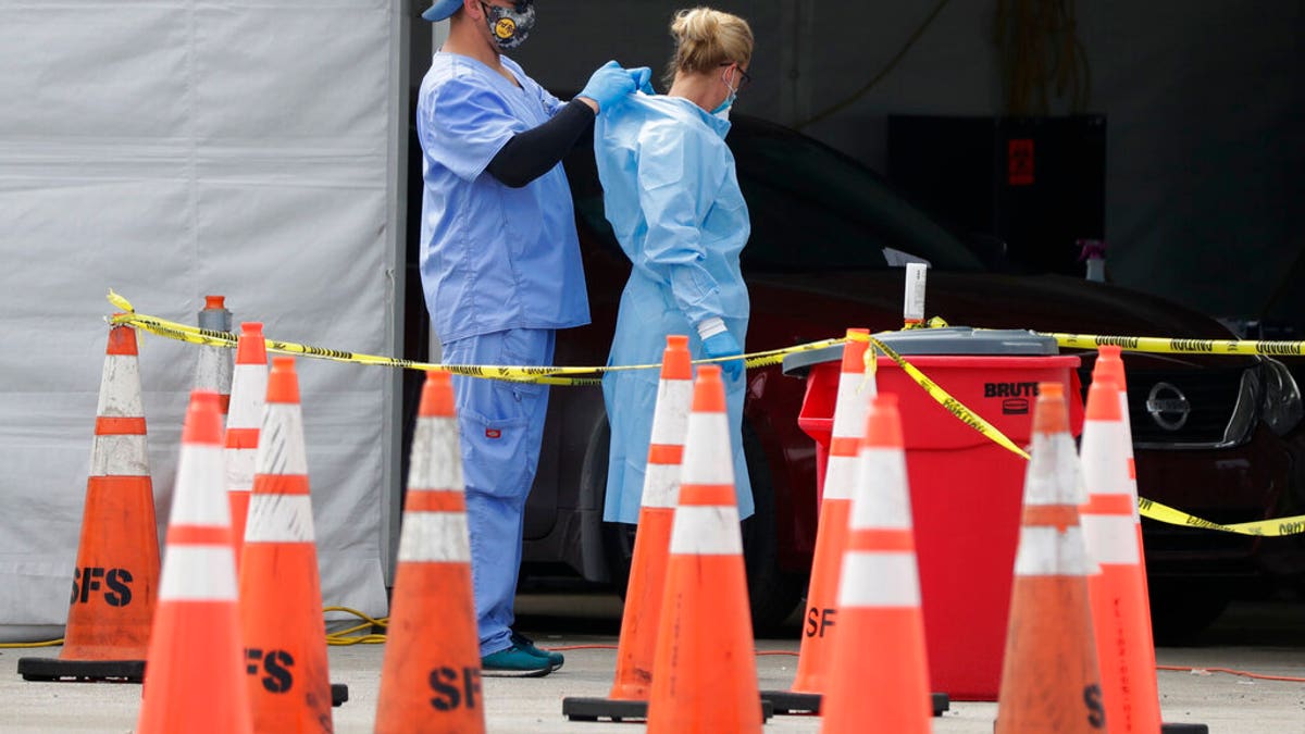 In this July 5, 2020, file photo, healthcare workers help each other with their personal protective equipment at a drive-thru coronavirus testing site outside Hard Rock Stadium in Miami Gardens, Fla.