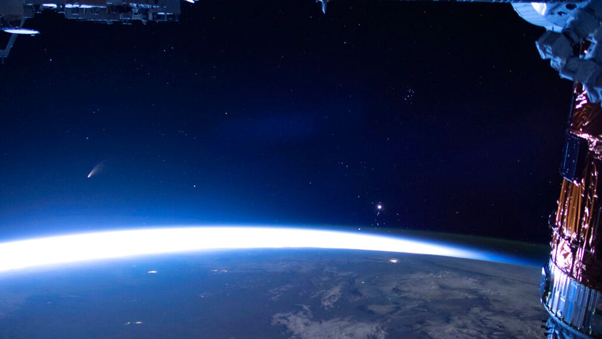 In this image released by NASA, Comet Neowise, left, is seen in the eastern horizon above Earth in this image taken from the International Space Station on Sunday, July 5, 2020. (NASA via AP)
