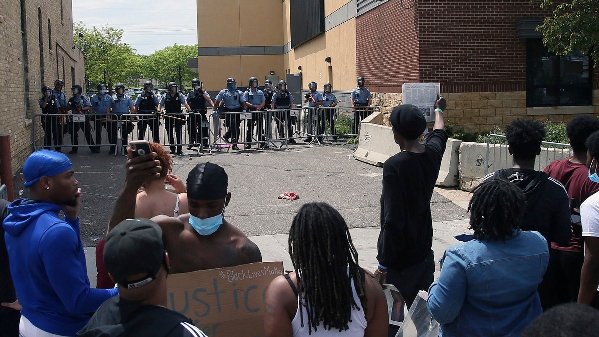 A protester holds a newspaper in front of the Minneapolis police standing guard against protesters at the Third Precinct as people protest the arrest and death of George Floyd on May 27, 2020. (AP Photo/Jim Mone, File)