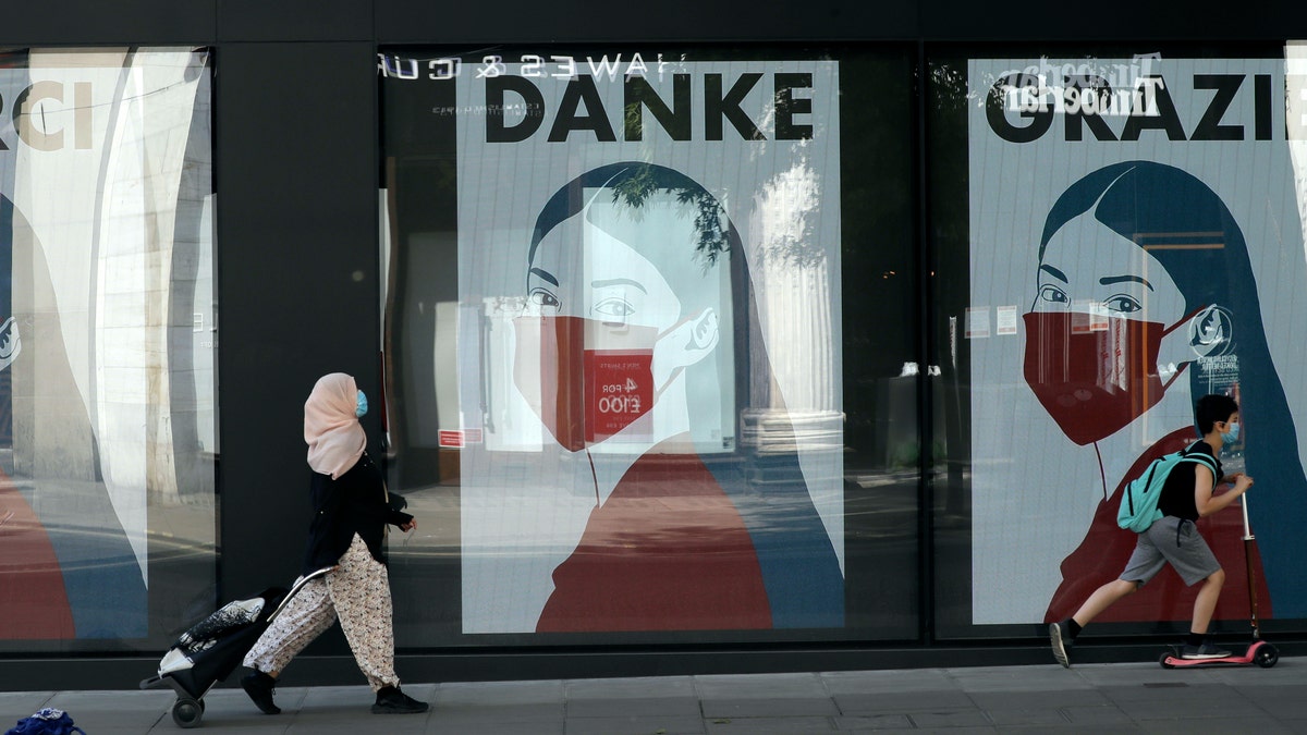 A woman and child wearing face masks past a coronavirus related artwork displayed on screens in the window of the Flannels clothing store on Oxford Street, in central London, Thursday, May 21, 2020. (AP Photo/Matt Dunham)
