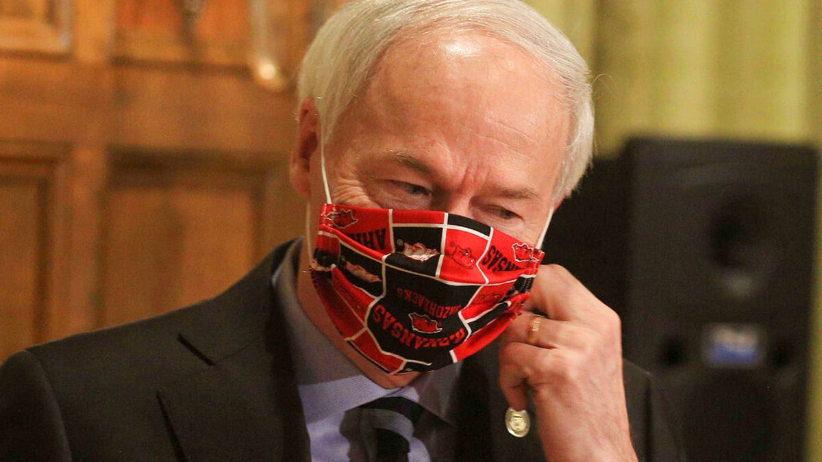 FILE: Gov. Asa Hutchinson takes off his Arkansas Razorbacks facemark as he arrives for the daily coronavirus briefing at the state Capitol in Little Rock.