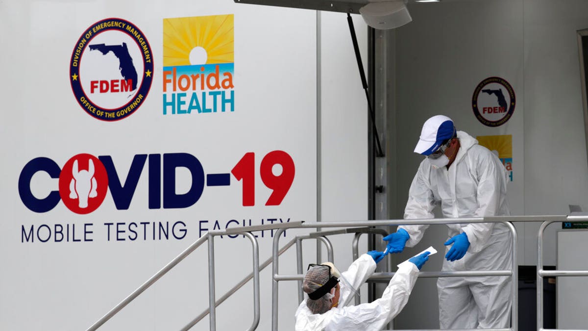 Health care workers work at a walk-up COVID-19 testing site during the coronavirus pandemic, Friday, July 17, 2020, in Miami Beach, Fla. People getting tested are separated from nurses via a glass pane. 