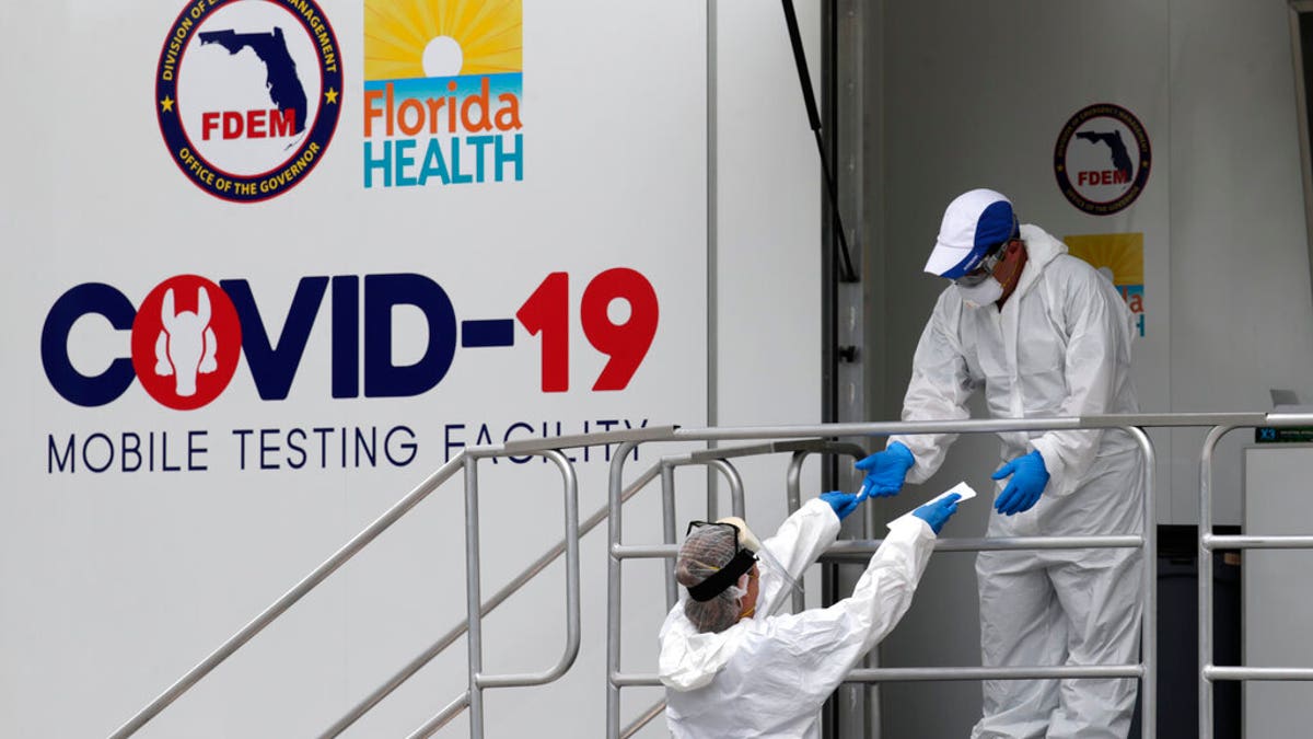 Health care workers work at a walk-up COVID-19 testing site during the coronavirus pandemic, Friday, July 17, 2020, in Miami Beach, Fla. People getting tested are separated from nurses via a glass pane.