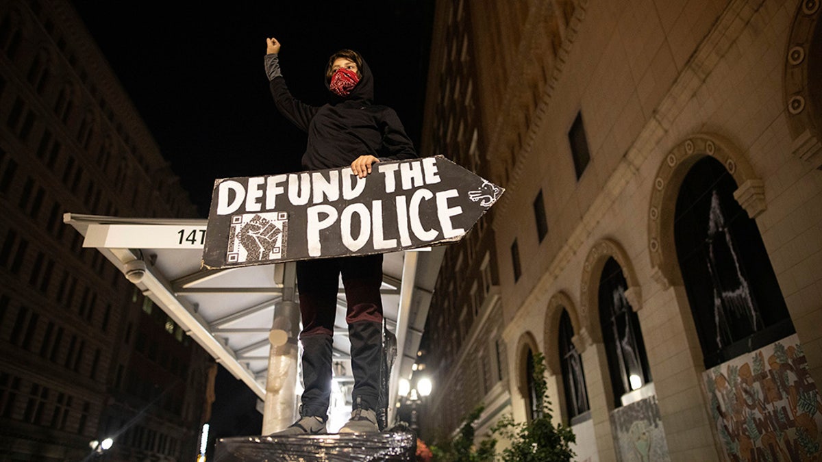 A protester holds a sign calling for the defunding of police at a protest on Saturday, July 25, 2020, in Oakland, Calif. Protesters in California set fire to a courthouse, damaged a police station and assaulted officers after a peaceful demonstration intensified late Saturday, Oakland police said. (AP Photo/Christian Monterrosa)