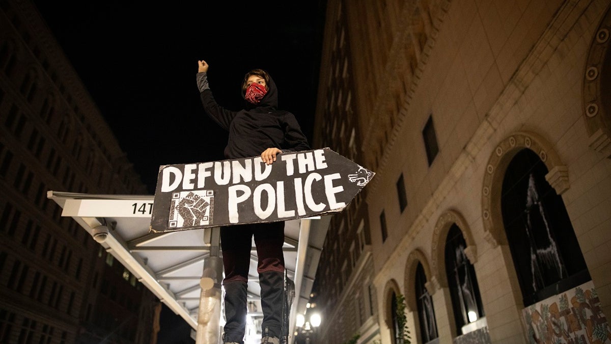 A protester holds a sign calling for the defunding of police at a protest on Saturday, July 25, 2020, in Oakland, Calif. Protesters in California set fire to a courthouse, damaged a police station and assaulted officers after a peaceful demonstration intensified late Saturday, Oakland police said. (AP Photo/Christian Monterrosa)