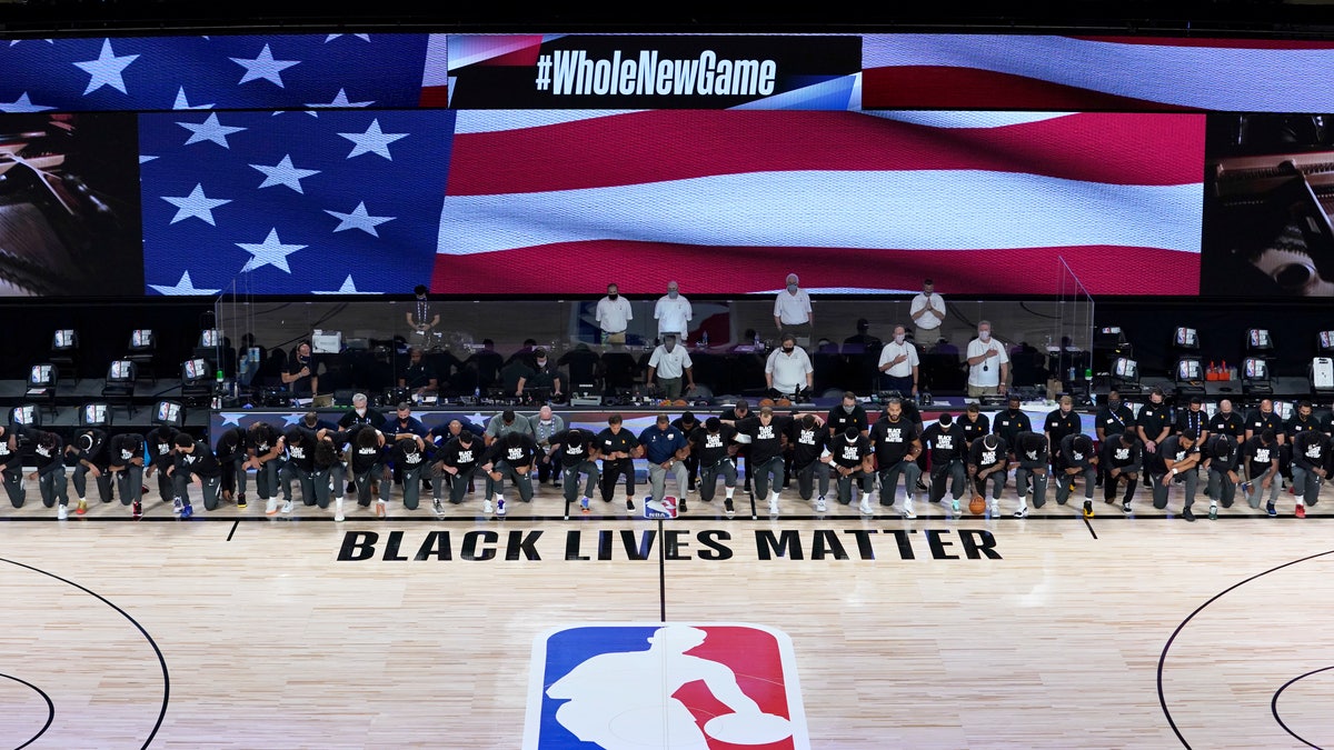 Members of the New Orleans Pelicans and Utah Jazz kneel together around the Black Lives Matter logo on the court during the national anthem before the start of an NBA basketball game Thursday, July 30, 2020, in Lake Buena Vista, Fla. (AP Photo/Ashley Landis, Pool)
