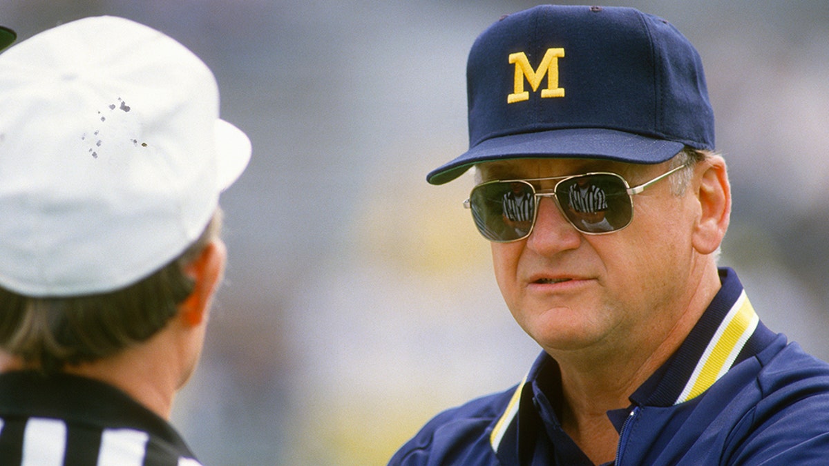 Head Coach Bo Schembechler of the Michigan Wolverines talks with an official while his team warms up before the start of an NCAA football game circa 1986.