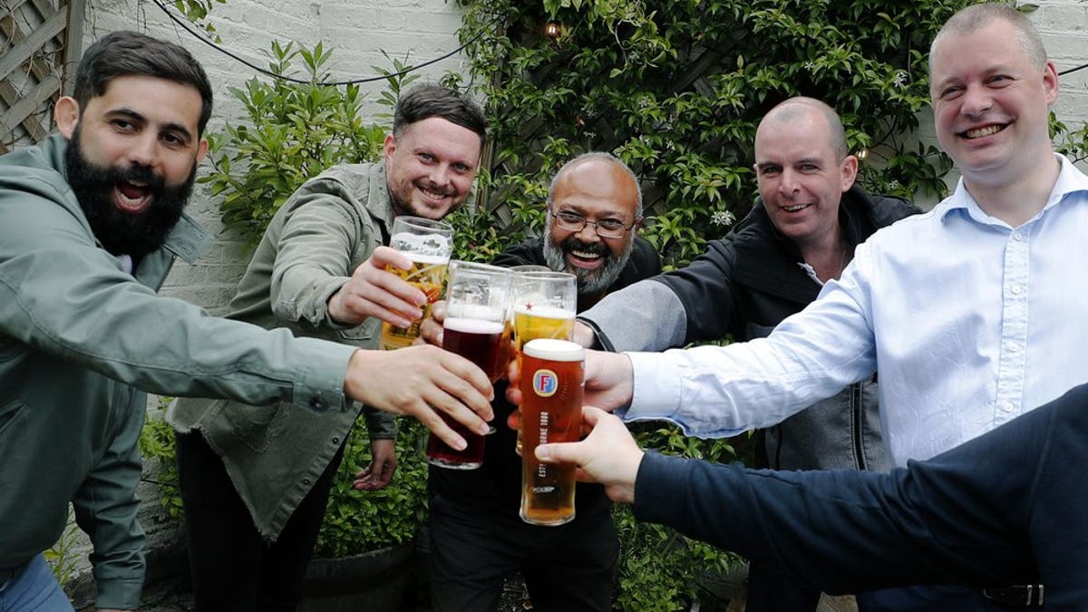 Men enjoy their first beers as the Chandos Arms pub reopens, in London, Saturday, July 4, 2020. England is embarking on perhaps its biggest lockdown easing yet as pubs and restaurants have the right to reopen for the first time in more than three months. In addition to the reopening of much of the hospitality sector, couples can tie the knot once again, while many of those who have had enough of their lockdown hair can finally get a trim.