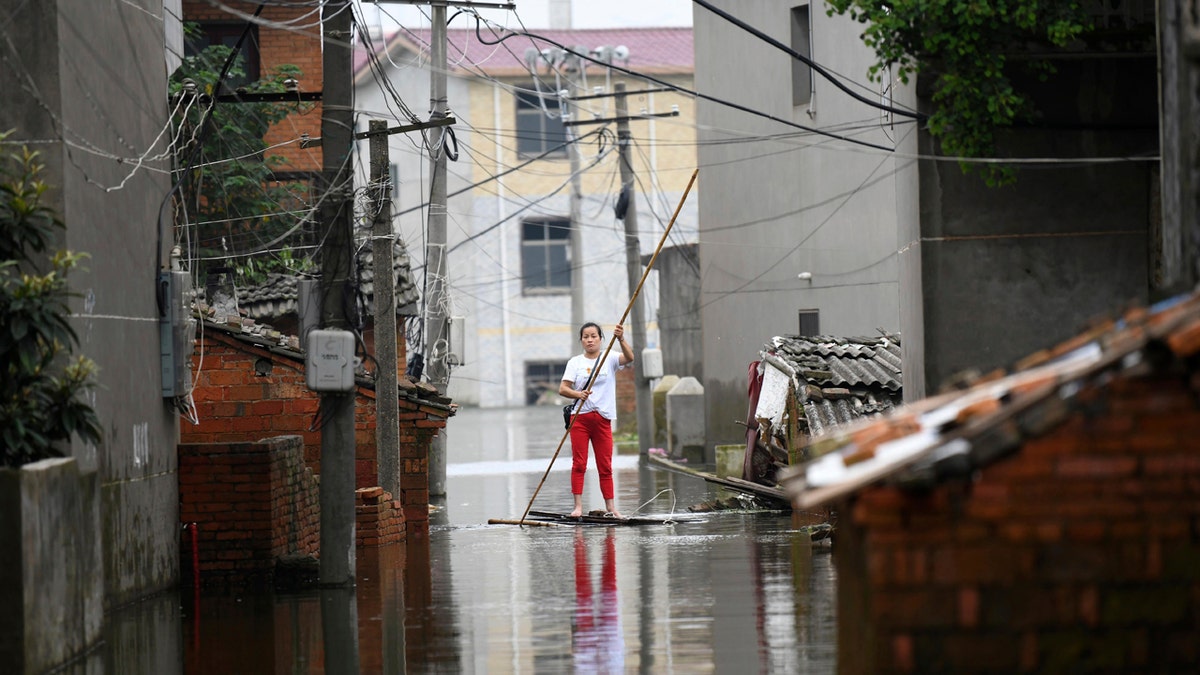 A woman pushes a makeshift raft down a flooded alleyway in a village in Yongxiu in central eastern China's Jiangxi province, Thursday, July 16, 2020.