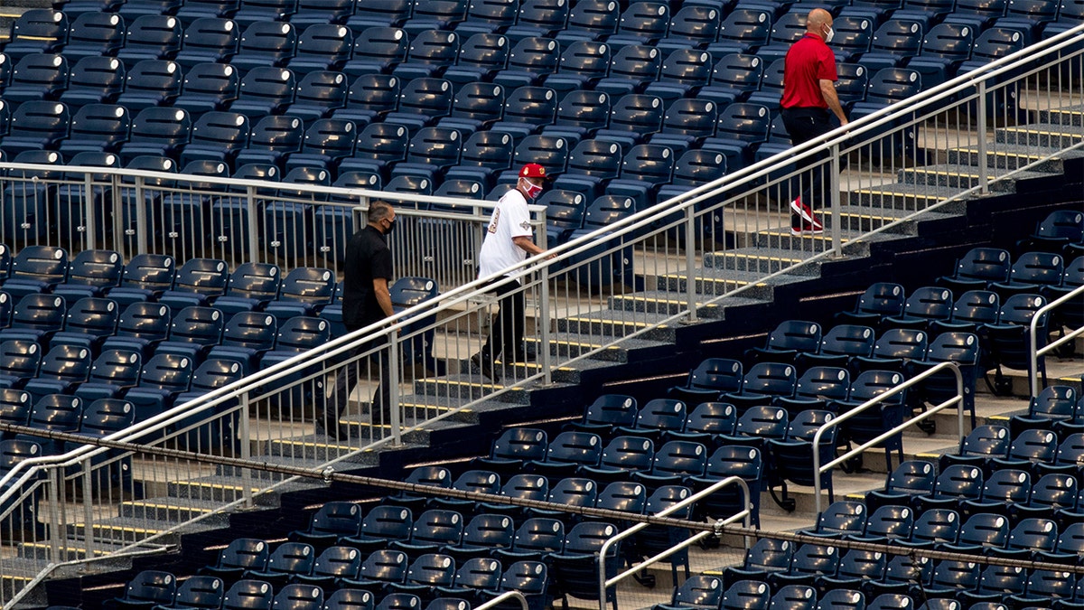 Director of the National Institute of Allergy and Infectious Diseases Dr. Anthony Fauci, center, walks through empty stands after throwing out the ceremonial first pitch at Nationals Park before the New York Yankees and the Washington Nationals play an opening day baseball game, Thursday, July 23, 2020, in Washington. (AP Photo/Andrew Harnik)