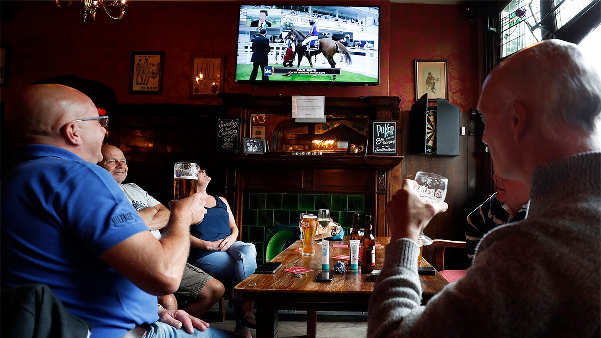 People enjoy their beers as they watch horse racing at the Forester pub in London, Saturday, July 4, 2020. England is embarking on perhaps its biggest lockdown easing yet as pubs and restaurants have the right to reopen for the first time in more than three months. In addition to the reopening of much of the hospitality sector, couples can tie the knot once again, while many of those who have had enough of their lockdown hair can finally get a trim. (AP Photo/Frank Augstein)