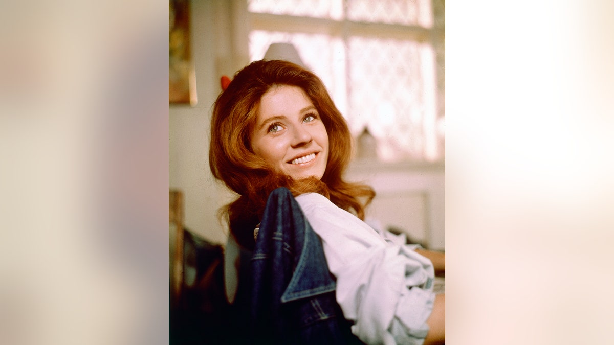 Patty Duke, US actress, smiling as she turns her head toward the camera for a portrait, while sitting in a chair with a denim jacket on the backrest, circa 1970.