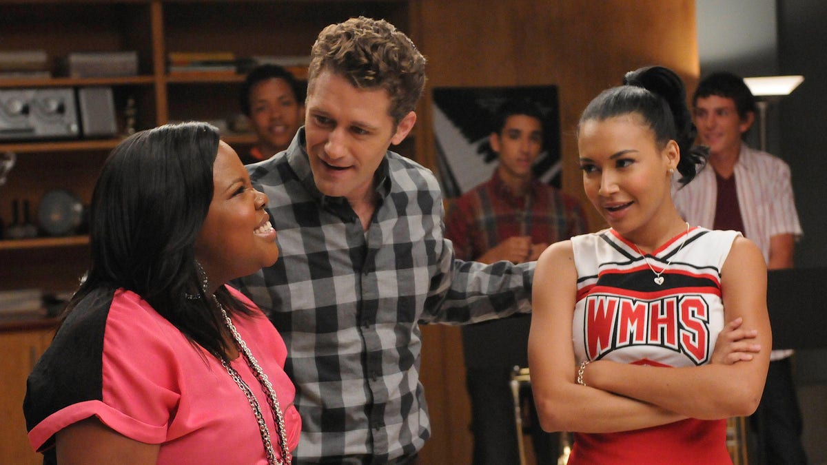 Will (Matthew Morrison, C) assigns Mercedes (Amber Riley, L) and Santana (Naya Rivera, R) a duet in the "Duets" episode.