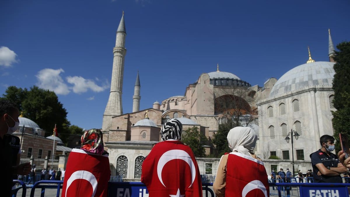 People, draped in Turkish flags, gather outside the Byzantine-era Hagia Sophia, one of Istanbul's main tourist attractions in the historic Sultanahmet district of Istanbul, following Turkey's Council of State's decision, Friday, July 10, 2020.