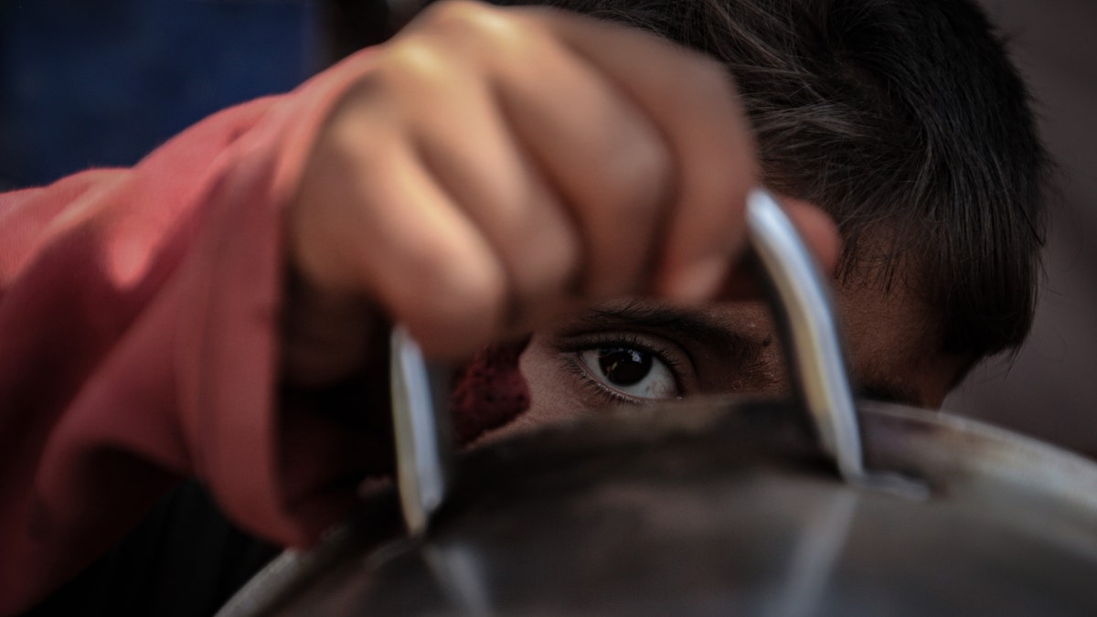 A Syrian boy looks through the handle of a cooking bowl as people queue to receive food aid in Idlib, Syria on October 07, 2019 - file photo.