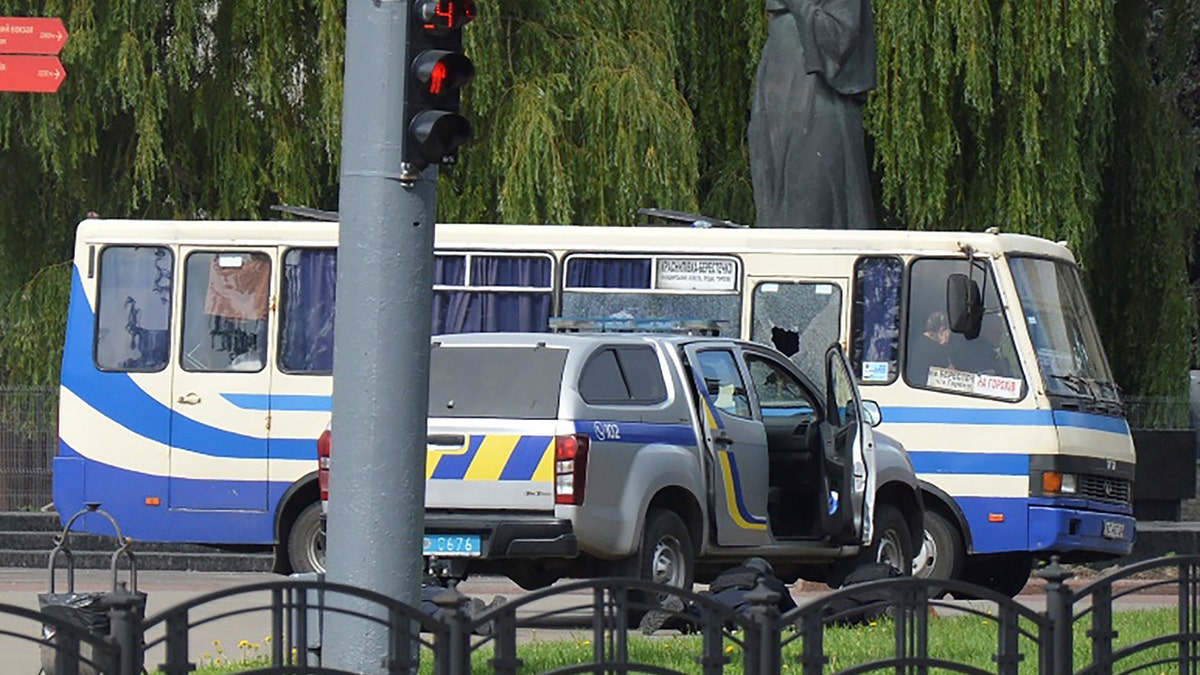 Ukrainian law enforcement officers lie on the ground behind a car near a passenger bus, which was seized by an unidentified person in the city of Lutsk, Ukraine July 21, 2020. (Reuters/Tetiana Hrishyna)