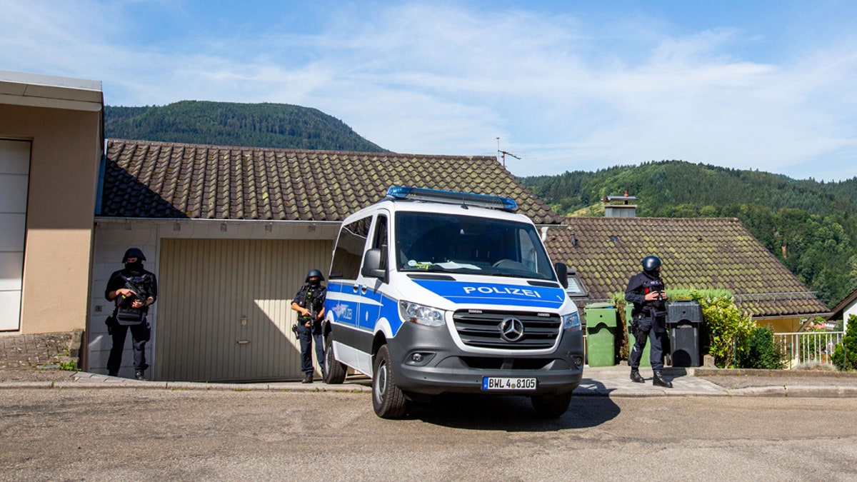 Police officers stay next to a police car in Oppenau, Germany, Monday, July 13, 2020. Authorities in Germany say they have deployed hundreds of police in the hunt for a 31-year-old man who disarmed four officers at gunpoint on Sunday, July 12, 2020. (Philipp von Ditfurth/dpa via AP)