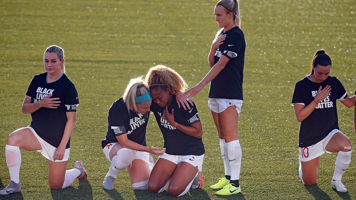 Chicago Red Stars' Julie Ertz, second from left, holds Casey Short, center, while other players for the team kneel during the national anthem before an NWSL Challenge Cup soccer match against the Washington Spirit at Zions Bank Stadium, Saturday, June 27, 2020, in Herriman, Utah. (AP Photo/Rick Bowmer)