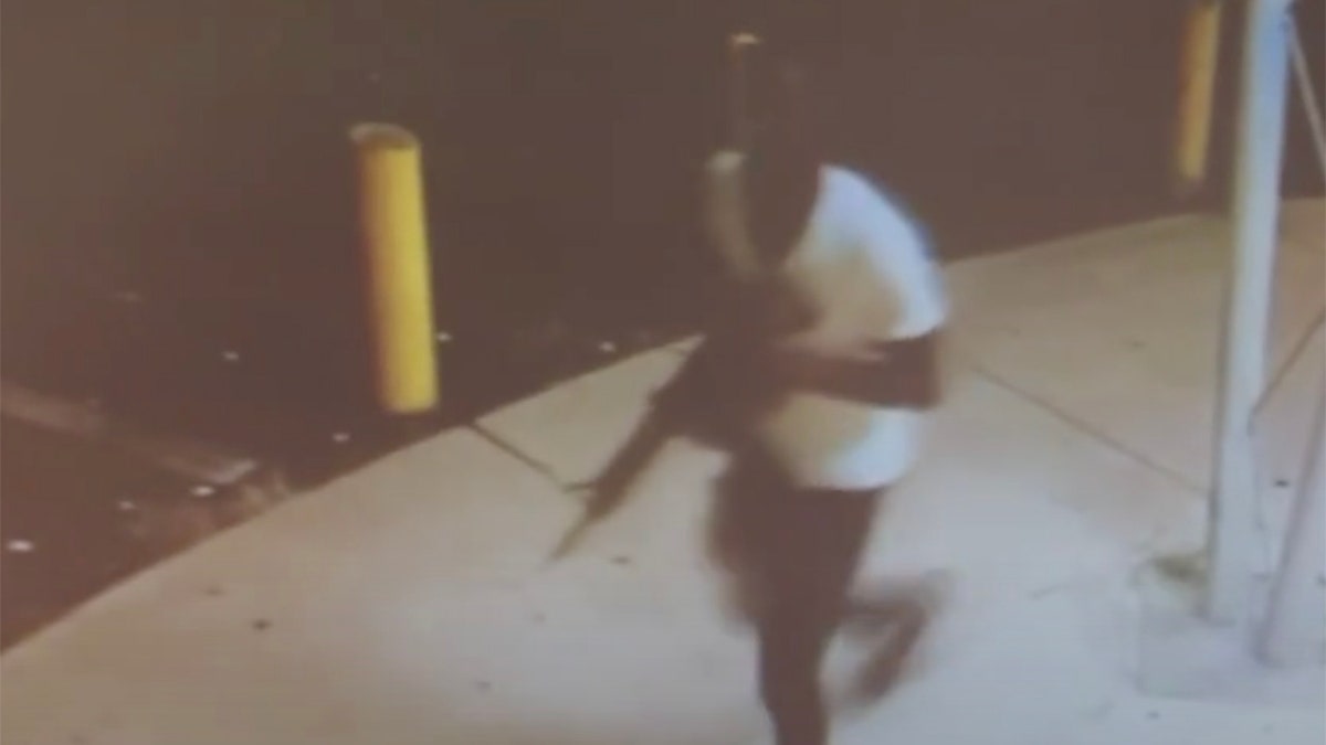 Newly released surveillance video shows a dark-skinned man wearing a white T-shirt and black pants as he walks with a rifle. 