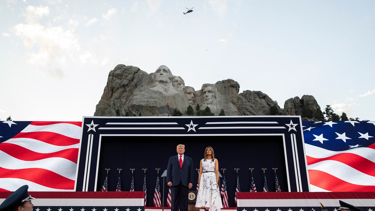 President Donald Trump, accompanied by first lady Melania Trump, stand during a flyover at Mount Rushmore National Memorial, Friday, July 3, 2020, near Keystone, S.D. (AP Photo/Alex Brandon)