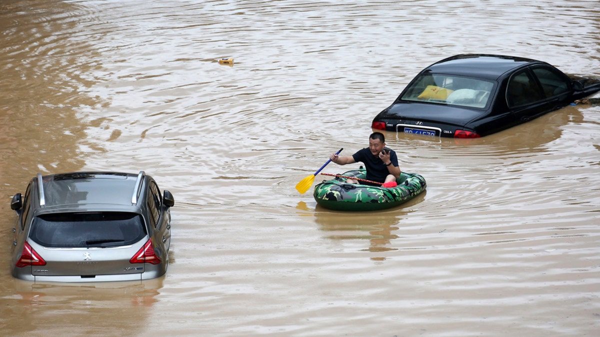 In this photo released by Xinhua News Agency, a man paddles with an inflatable boat past submerged cars during a flood in Rongshui County in southern China's Guangxi Zhuang Autonomous Region, July 11.