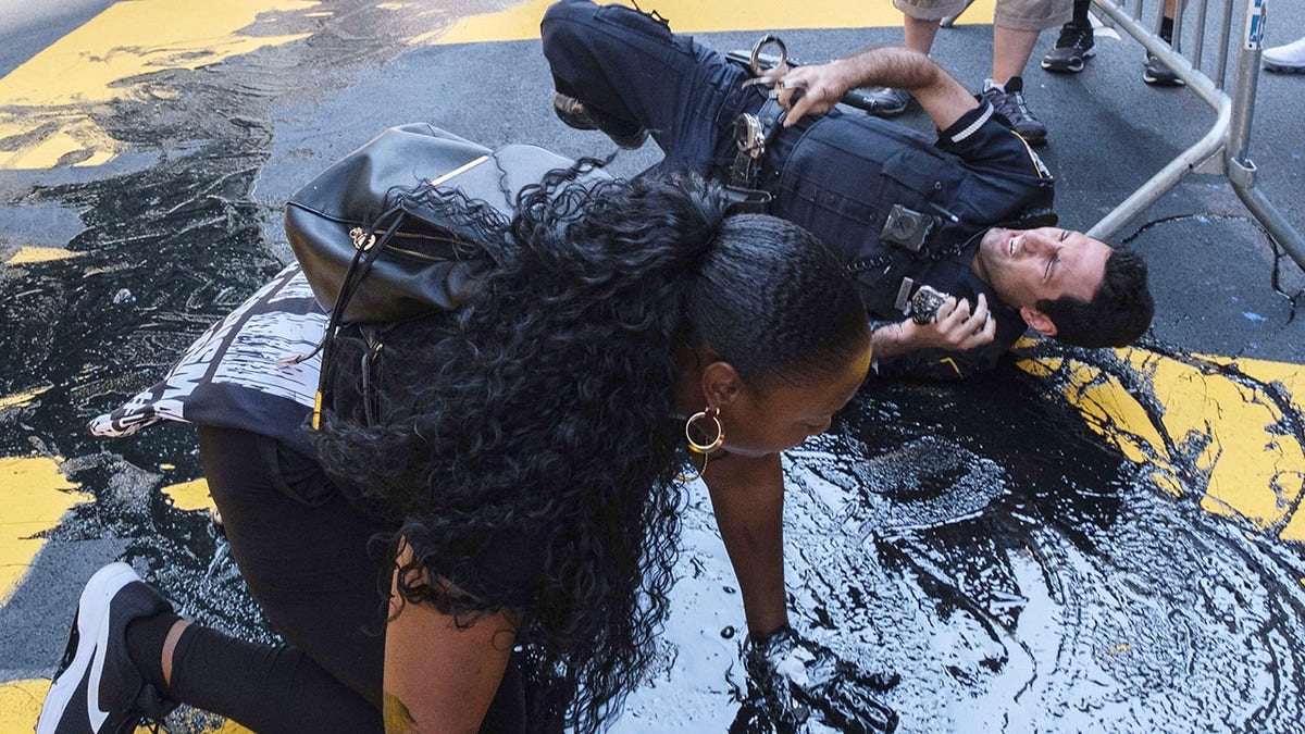 An NYPD officer slips and falls during an attempt to detain a protester pouring black paint on the Black Lives Matter mural outside of Trump Tower on Fifth Avenue in the Manhattan borough of New York on Saturday. (AP Photo/Yuki Iwamura)