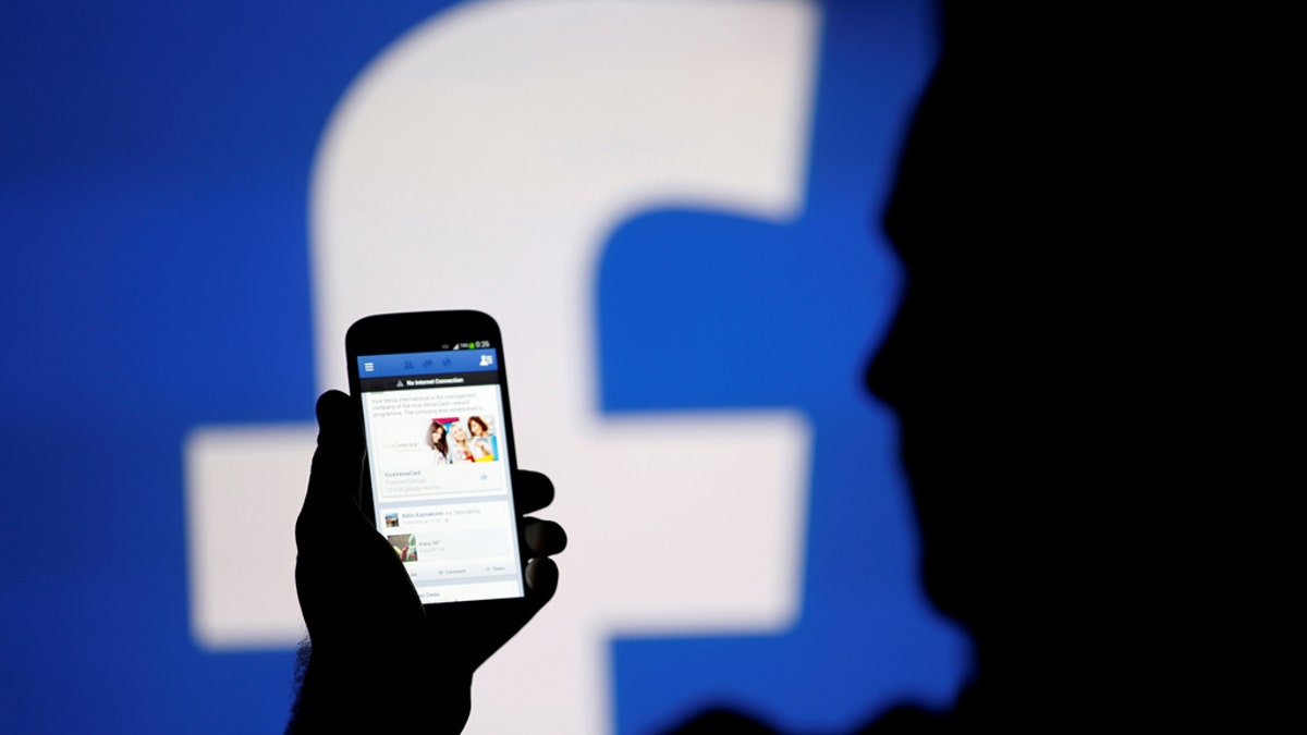 A man is silhouetted against a video screen with a Facebook logo. REUTERS/Dado Ruvic 