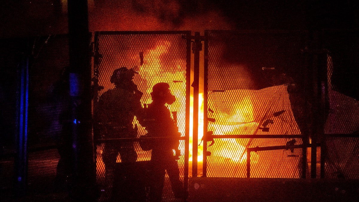 Federal officers guard the Mark O. Hatfield U.S. Courthouse as a fire lit by protesters burns on the other side of a perimeter fence in Portland during July 2020. (AP Photo/Noah Berger)