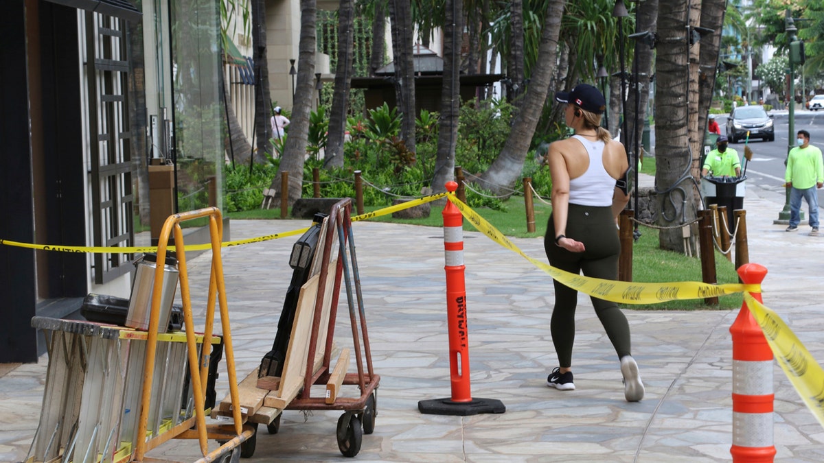 A woman walks past boarded storefronts in the Waikiki neighborhood of Honolulu, Saturday, July 25, 2020, as Hurricane Douglas approaches.