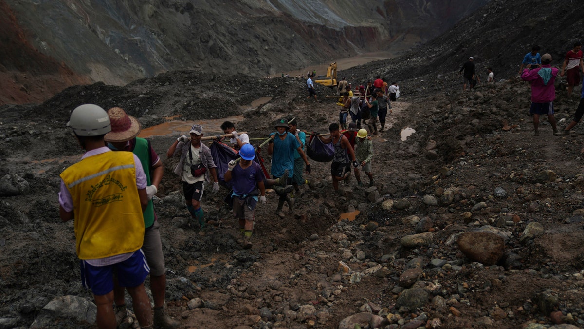 Rescue workers use poles to carry bodies shrouded in blue and red plastic sheets July 2, in Hpakant, Kachin State, Myanmar.