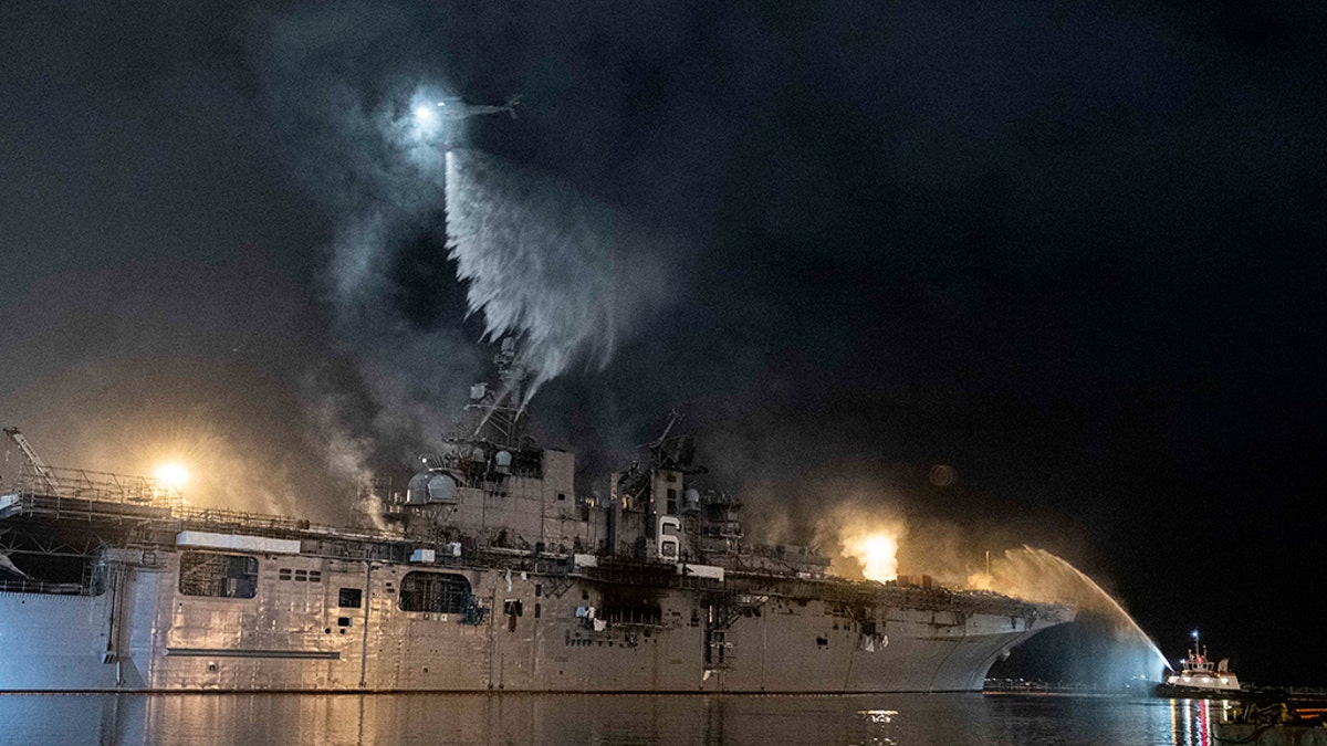 A helicopter from Helicopter Sea Combat Squadron (HSC) 3 combats a fire aboard the amphibious assault ship USS Bonhomme Richard (LHD 6) at Naval Base San Diego, Tuesday, July 14, 2020. A Navy statement says there's been significant progress and much less smoke is being emitted from the USS Bonhomme Richard on Tuesday. (Mass Communications Specialist 3rd Class Garrett LaBarge/U.S. Navy via AP)