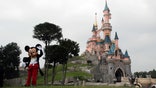 FILE - In this June 8, 2018 file photo, a person dressed as Mickey Mouse poses in front of the castle of Sleeping Beauty at Disneyland Paris, in Chessy, France, east of Paris. The French tourist industry received a further boost Wednesday, July 15, 2020 with the partial reopening of Disneyland Paris and the opening up of the top floor of the Eiffel Tower. Disneyland Paris, Europe’s most frequented theme park resort, is partially re-opening to the public, four months after it closed as a result of the coronavirus pandemic. (AP Photo/Francois Mori, File)