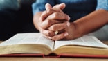 Closeup of an unrecognizable person's hands held over a bible at home during the day