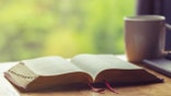 Open bible with a cup of coffee for morning devotion on wooden table with window light