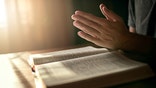 Cropped shot of an unidentifiable man clasping his hands in prayer over an open Bible