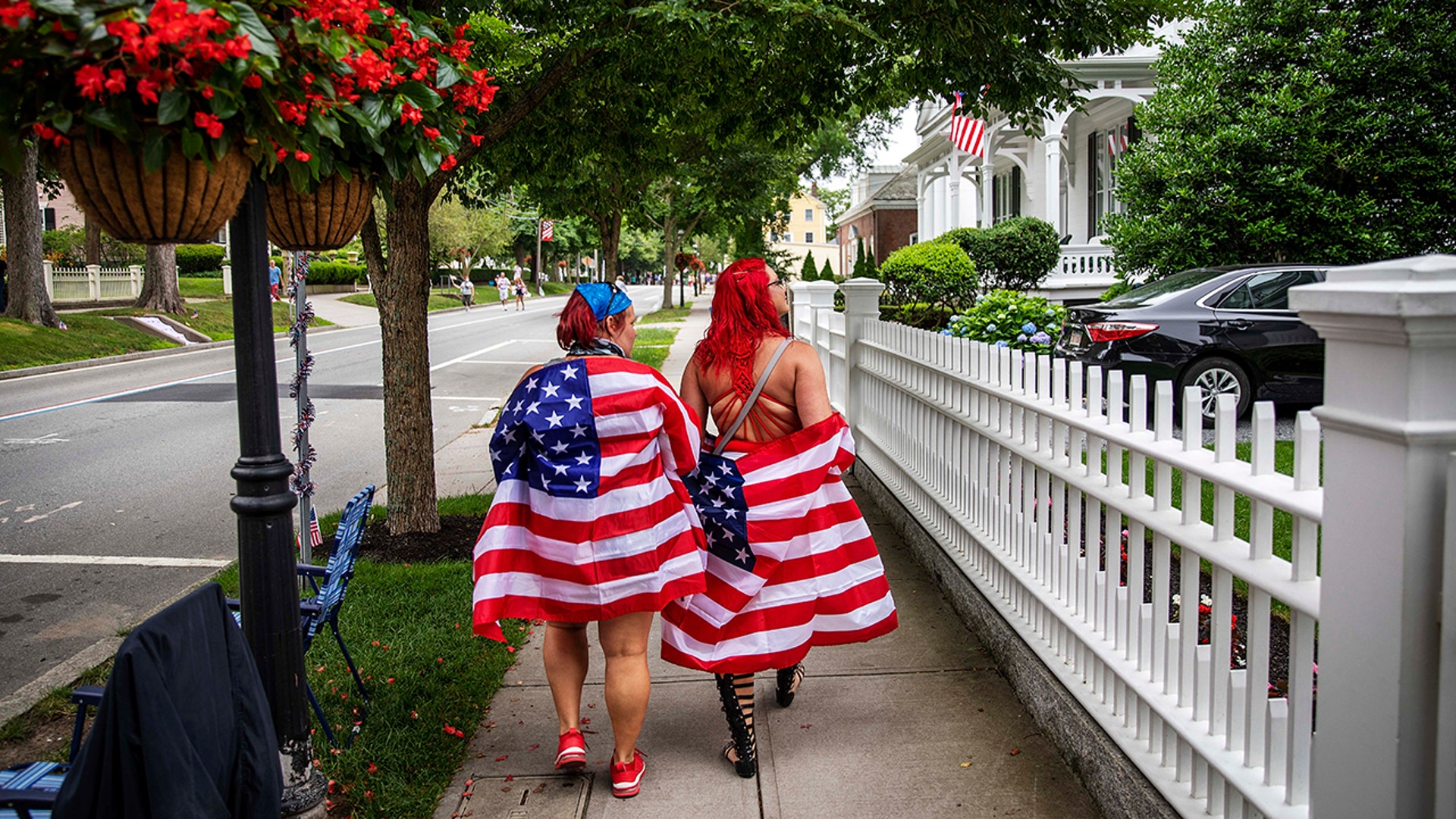 Parade-goers draped in American flags walk down the street before a Fourth of July parade in Bristol, Rhode Island, July 4, 2020.