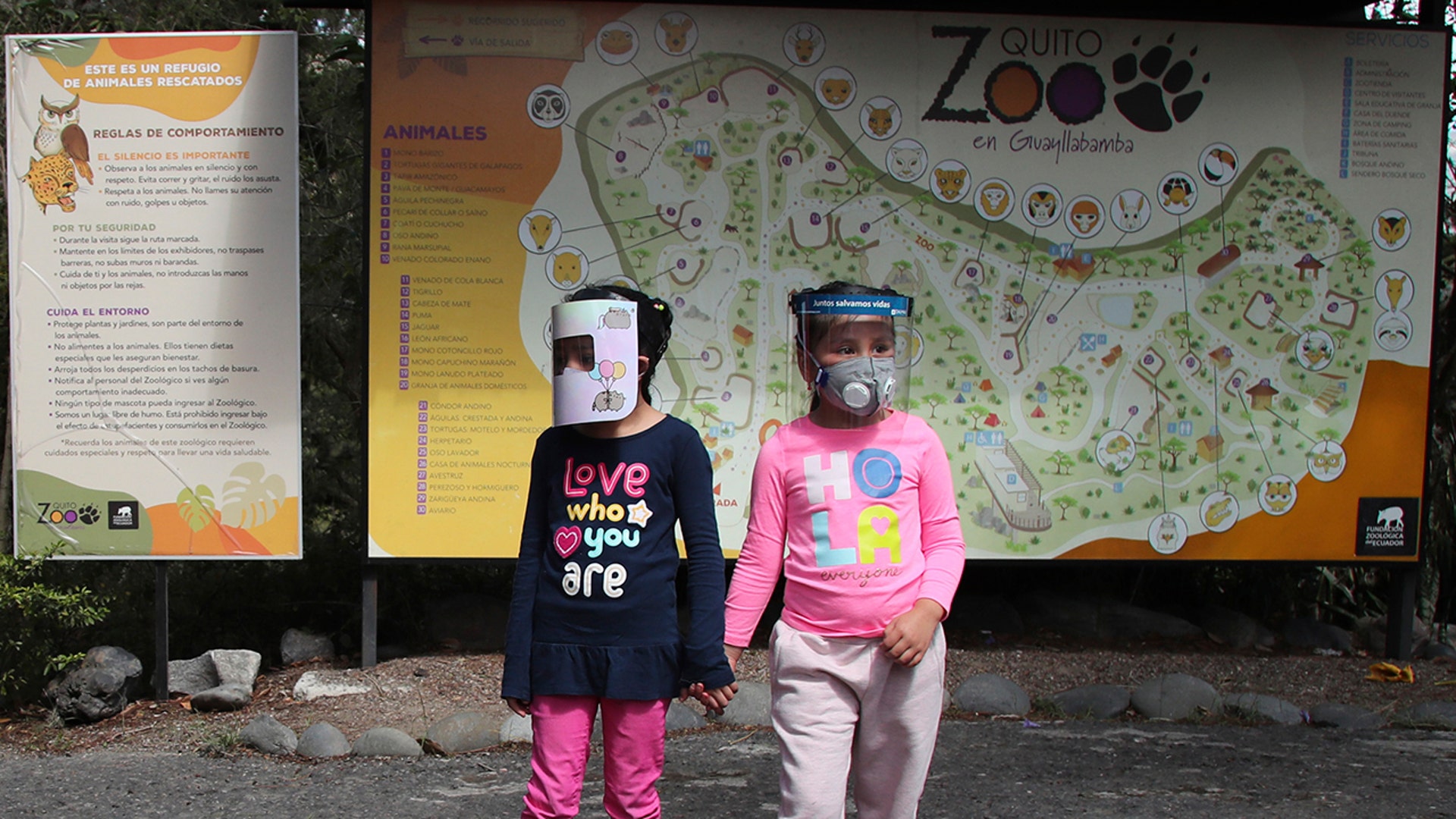Girls wearing face shields as a preventive measure against the coronavirus wait for their parents to enter the zoo in Quito, Ecuador, July 8, 2020.