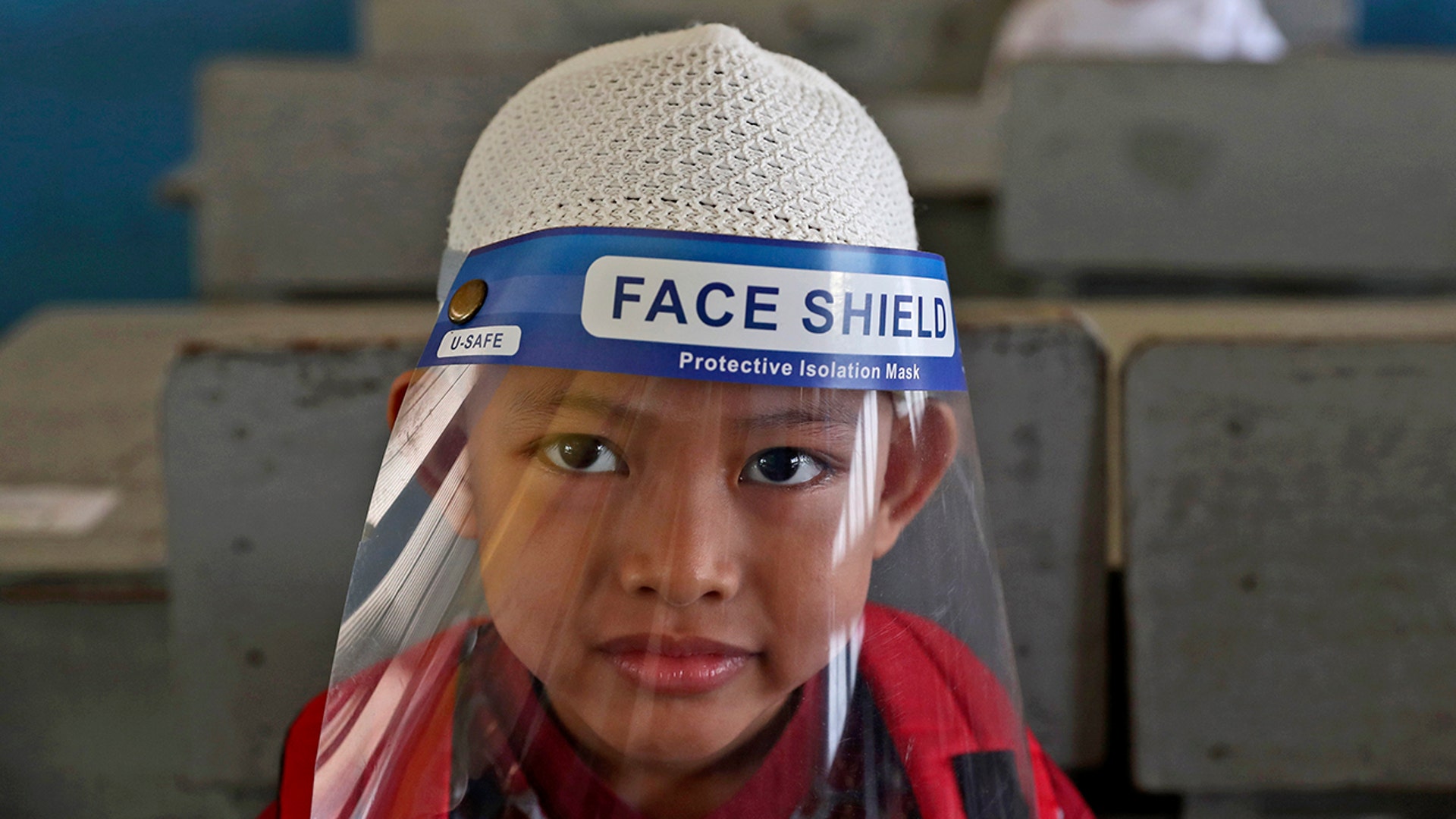 A young boy wearing a face shield as a precaution against the coronavirus waits his turn to take an admission test at Al Hidayah Islamic Elementary School in Jakarta, Indonesia, July 6, 2020. 