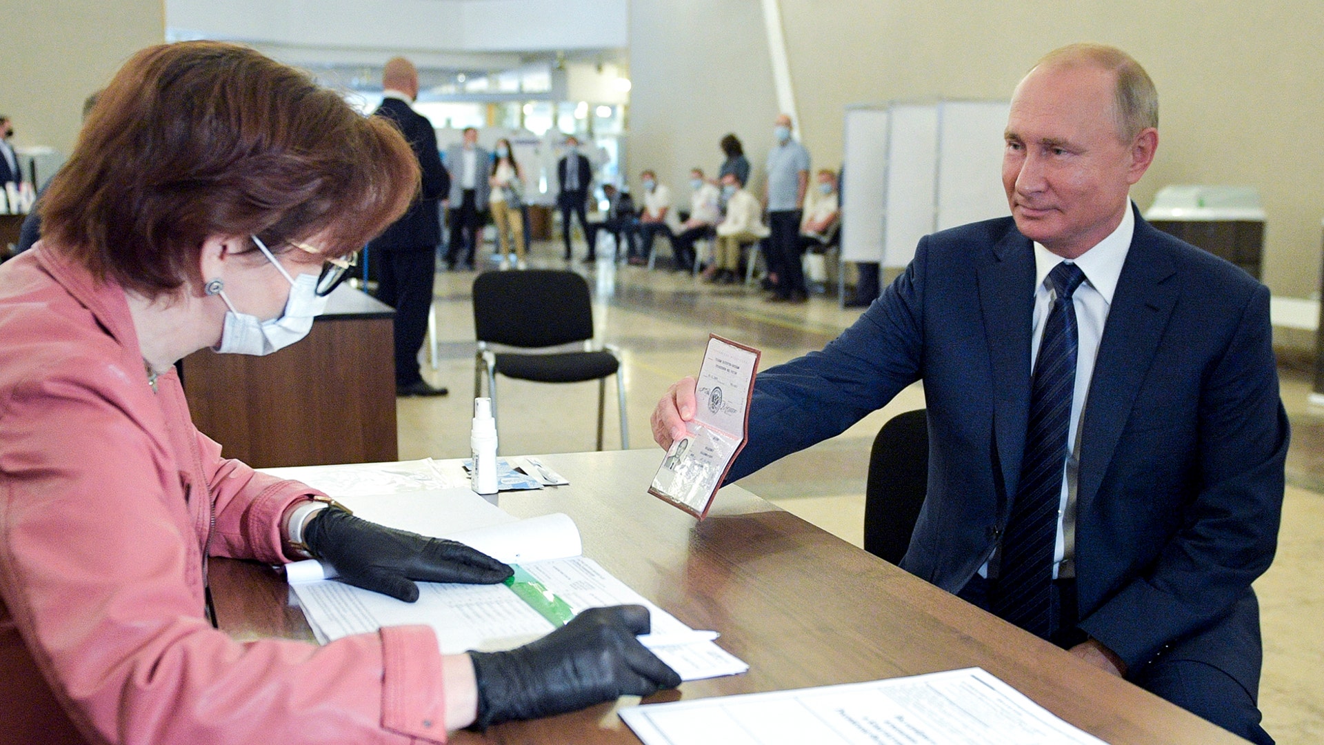 Russian President Vladimir Putin shows his passport to a member of an election commission as he arrives to take part in voting at a polling station in Moscow, Russia, July 1, 2020. 