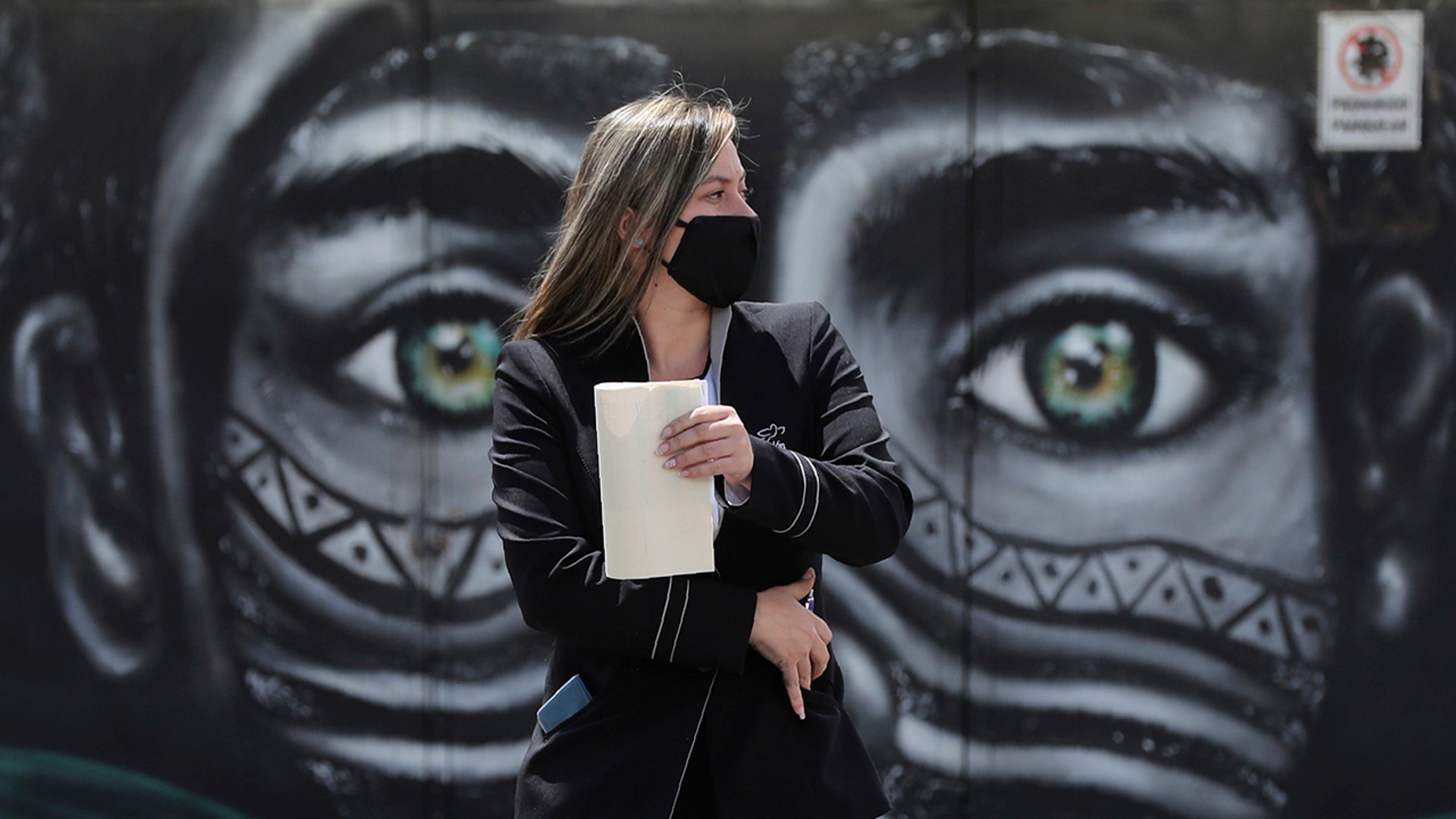 A woman wearing a face mask walks past a mural of an Indigenous man in Bogota, Colombia, July 3, 2020.