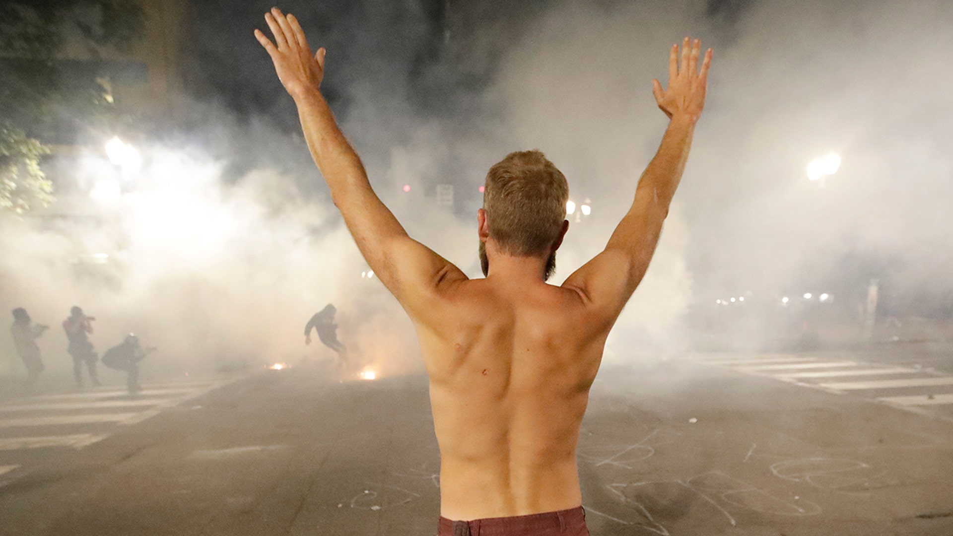 A demonstrator holds his arms up in the air as federal officers launch tear gas during a Black Lives Matter protest at the Mark O. Hatfield U.S. Courthouse Tuesday, July 28, 2020, in Portland, Ore.