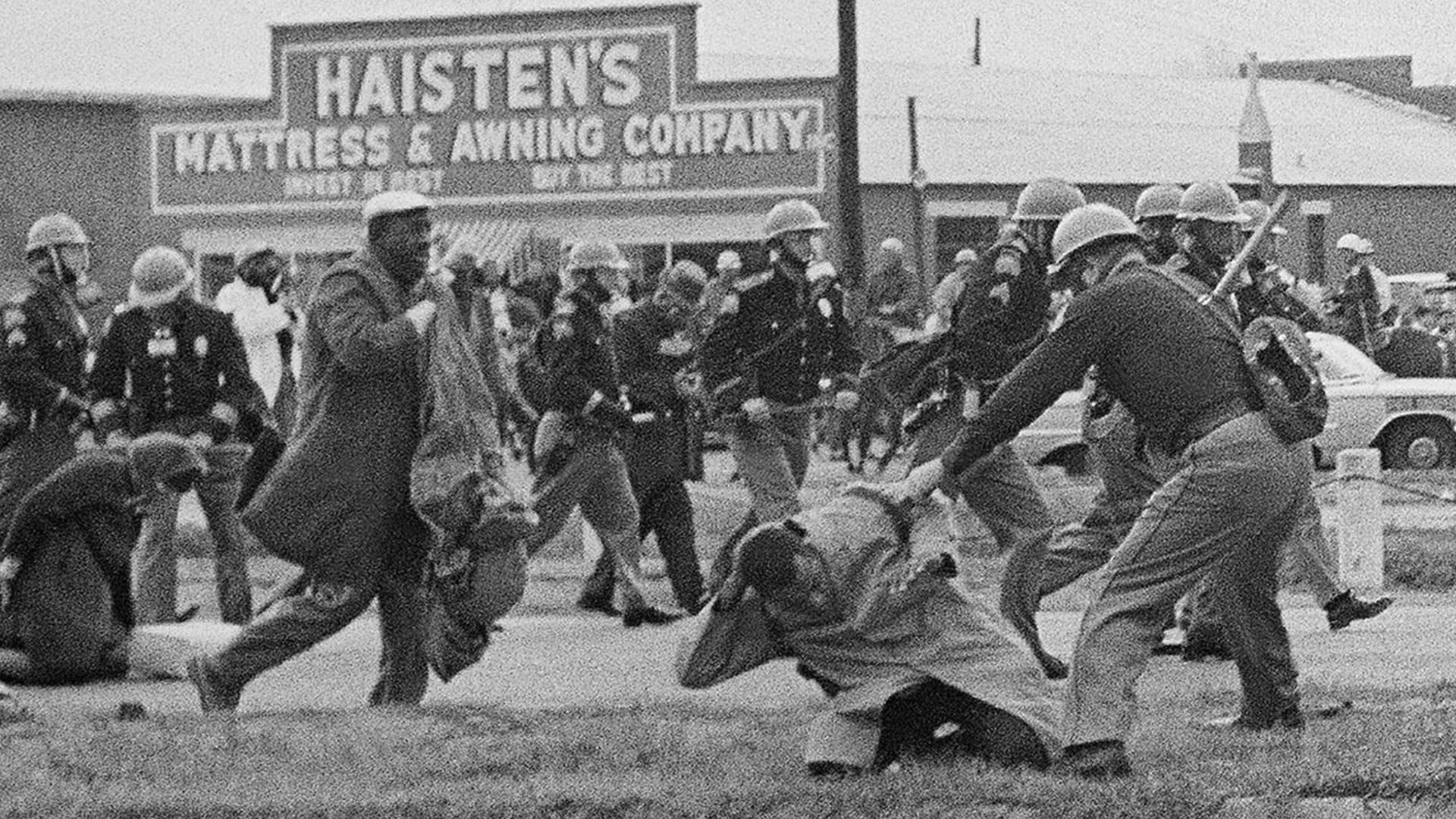 A state trooper swings a billy club at John Lewis, right foreground, chairman of the Student Nonviolent Coordinating Committee, to break up a civil rights voting march in Selma, AL, March 7, 1965.